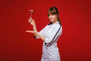 The doctor is holding a neurological hammer on a red background. The neurologist checks the patient's reflexes with a hammer. Diagnostics, healthcare, and medical care photo