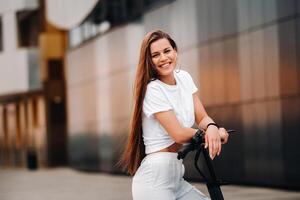 beautiful girl in white stylish clothes on an electric scooter in the city photo