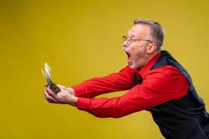 Portrait of super excited senior mature man who just won lots of money, trying to give or take money. Isolated on yellow background. Positive emotion facial expression feelings. Closeup photo