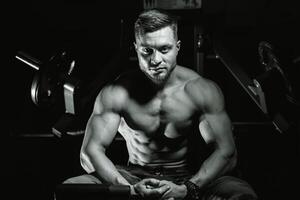 hermoso hombre con grande músculos, posando a el cámara en el gimnasia, negro y azul antecedentes. retrato de un sonriente carrocero. de cerca. foto