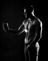 Photo of half naked sportsman holding sport bottle of water. Half turned to the camera. Black and white. Close-up.
