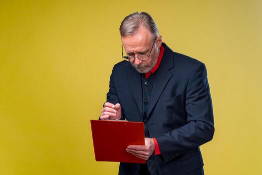 Middle aged businessman standing and holding file folder. Checking notes. Horizontal format isolated on yellow background. photo