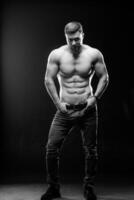 A portrait of a hot handsome strong guy man without a shirt against dark background. Hands on belt. Studio photo. Male beauty concept. Black and white photo. Closeup. photo