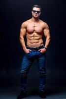 Muscular and fit young bodybuilder fitness male model posing over dark background. Full size photo. photo