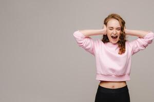 A beautiful girl on a gray background holds her head and screams emotionally photo