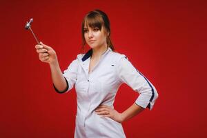 The doctor is holding a neurological hammer on a red background. The neurologist checks the patient's reflexes with a hammer. Diagnostics, healthcare, and medical care photo