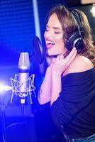 Shot of a pretty young woman in headphones singing a song with a microphone. Shot in a studio. Vocalist female portrait photo