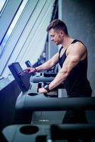 Sporty strong man training cardio in the gym. Male runner on treadmill in gym doing cardio workout. photo