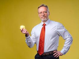 An old man with a beard holds out a yellow apple. Isolated on yellow background. photo