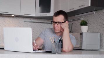 Young man in glasses works from home sitting at the table using laptop makes a report video