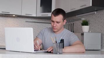 Young male specialist is having difficulty working remotely from home and holds his hands behind his head while sitting at a table. video