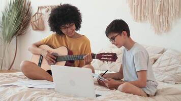 música enseñando, musical educación, jugando guitarra, hora juntos. mujer enseña chico a jugar guitarra utilizando ordenador portátil. video