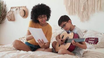 música enseñando, musical educación, jugando guitarra, hora juntos. mujer profesor enseña niño a jugar acústico guitarra utilizando notas video