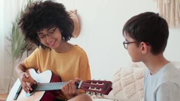 musica insegnamento, musicale formazione scolastica, giocando chitarra, tempo insieme. afro americano donna insegnamento ragazzo per giocare chitarra mentre seduta su letto a casa video