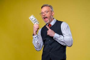 Closeup portrait of super excited senior mature man who just won lots of money, isolated on yellow background. Positive emotion facial expression feelings. photo