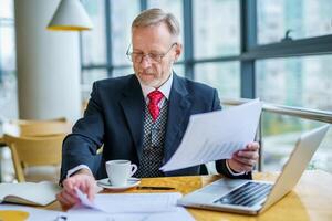 Businessman checks a printed report or document when he sits, working on paper work at a laptop. photo