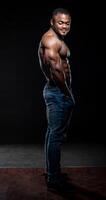 muy muscular afro americano hombre con desnudo torso poses en negro antecedentes. carrocero en pantalones mirando a el cámara foto