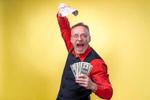 Man holding lots of dollar bills in hands, isolated on yellow background. Happy man enjoying money. Hands with money. Rich with success. Positive emotion facial expression feelings. photo