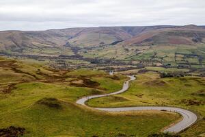 devanado la carretera mediante un lozano, verde Valle con laminación colinas debajo un nublado cielo en pico distrito, Inglaterra. foto