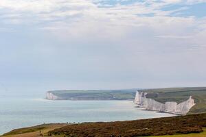 Scenic view of white chalk cliffs and calm sea with hazy sky, grassy foreground at Seven Sisters, England. photo