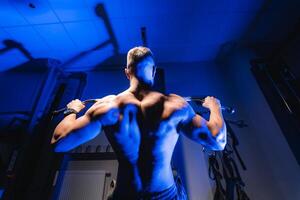 Athlete with strong body doing work out pushing up excercise in gym. View from the bottom. Blue light filter. photo