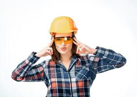 Pretty woman wearing orange protective helmet and glasses. Female holding fingers near head. Isolated on white background. Female builder in safety helmet photo