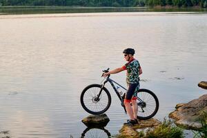 Mountain biker with a bicycle on a rock in a lake. Motivation and inspiration for adventure. Extreme sport concept. photo