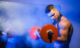 Fit young man lifting barbells doing workout at a gym. Sport, fitness, weightlifting, bodybuilding, training, athlete, workout exercises concept. View from the side. photo