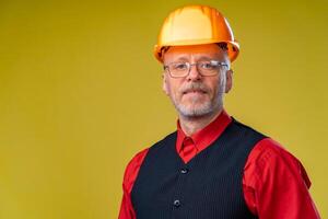 Positive senior engineer in a helmet on a yellow background. photo