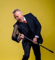 Senior man singing in mop. Serious man in suit having fun while cleaning the floor. photo