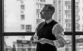 Man staying near big window. Businessman in suit thinking over ideas. Panoramic city view. Relaxing and taking break. Black and white photo. photo