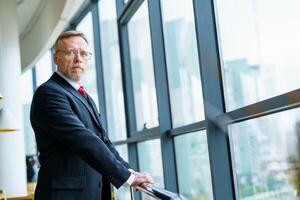 Portrait of a senior businessman standing against big windows background. Modern suit, photo