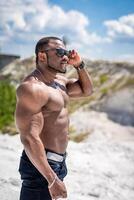 Muscular young bodybuilder with naked torso standing on landscapes. Strong healthy shirtless man. photo