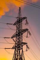 Metal electric pillar with orange sky background. Power transmission facilities. High voltage pylons against sunset background. Energy and industrialization concept. Selective focus photo