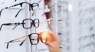 Selective focus on hand. Woman touching corrective glasses on stand with spectacles. Wide assortment in shop. photo