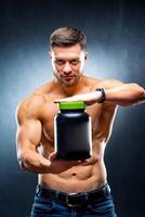 Male athlete bodybuilder holds a jar of sports nutrition in his hands showing to the camera poses on blue background. photo