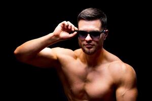 Well build handsome man without a shirt posing in studio. Strong body and cool face. Male wearing glasses. Portrait. Selective focus. Closeup. photo