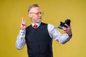 Senior man looking at camera in hands. Man taking selfie showing piece sign to the camera photo