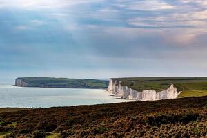 Scenic view of white chalk cliffs with lush greenery under a clear sky at the coast at Seven Sisters, England. photo