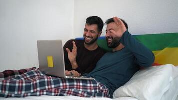 two men in pajamas on a bed with a laptop video