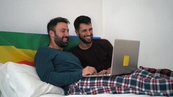 two men in pajamas on a bed with a laptop video