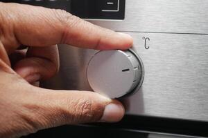 Close up of men hand setting temperature control on oven. photo