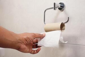 Hand pulling toilet paper roll in holder photo