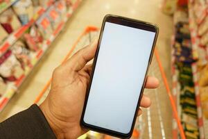 mano participación móvil teléfono con blanco pantalla mientras compras a supermercado. foto