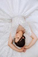 A brunette bride is lying on a lace dress, posing with closed eyes photo