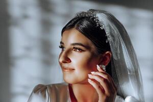 portrait of an incredibly beautiful girl bride in a white robe in the bedroom in beautiful light and shadow, the bride poses in the morning before the wedding ceremony. photo