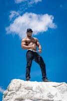 Handsome athletic man on the blue sky. Muscular strong bodybuilder posing for camera. photo