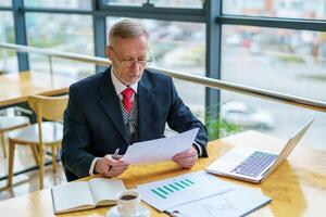 Thoughtful middle aged businessman in suit. Sitting near the window in office. Panoramic city view background. Business photo. photo