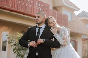 encantador y elegante recién casados son abrazando y sonriente en contra el antecedentes de otoño naturaleza en un hermosa jardín. un increíblemente hermosa joven novia inclinado en contra el hombro de su amado novio foto