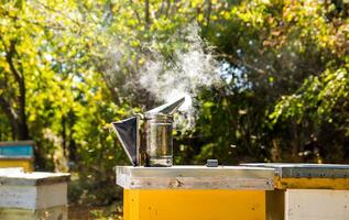 Bee smoker stands on yellow beehive. Steel instrument for pouring smoke in air. Apiculture concept. photo